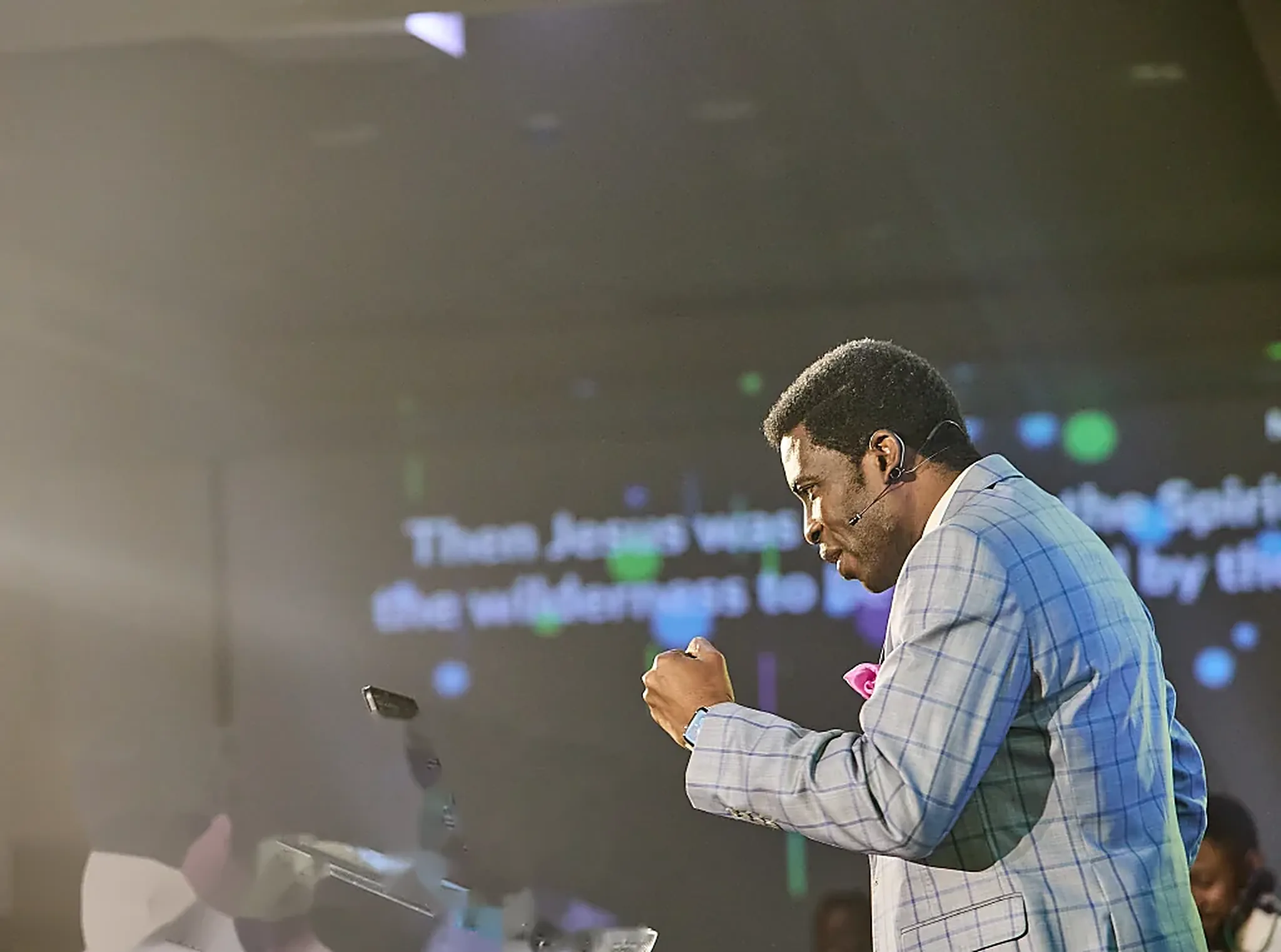 Pastor Dare Kolawole in a grey check suit, ministering at the lectern