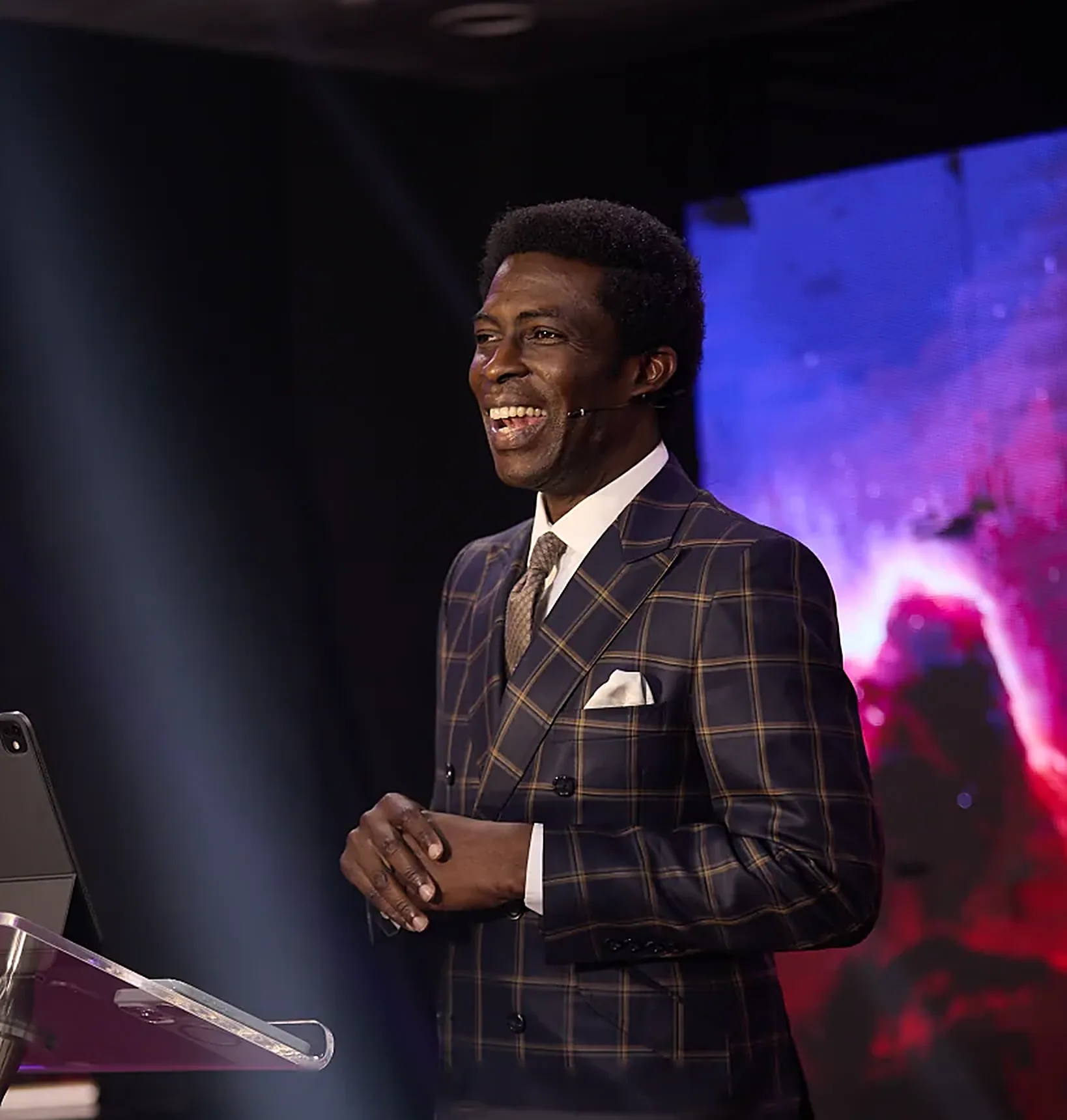 Pastor Dare Kolawole smiling in a navy and gold check suit