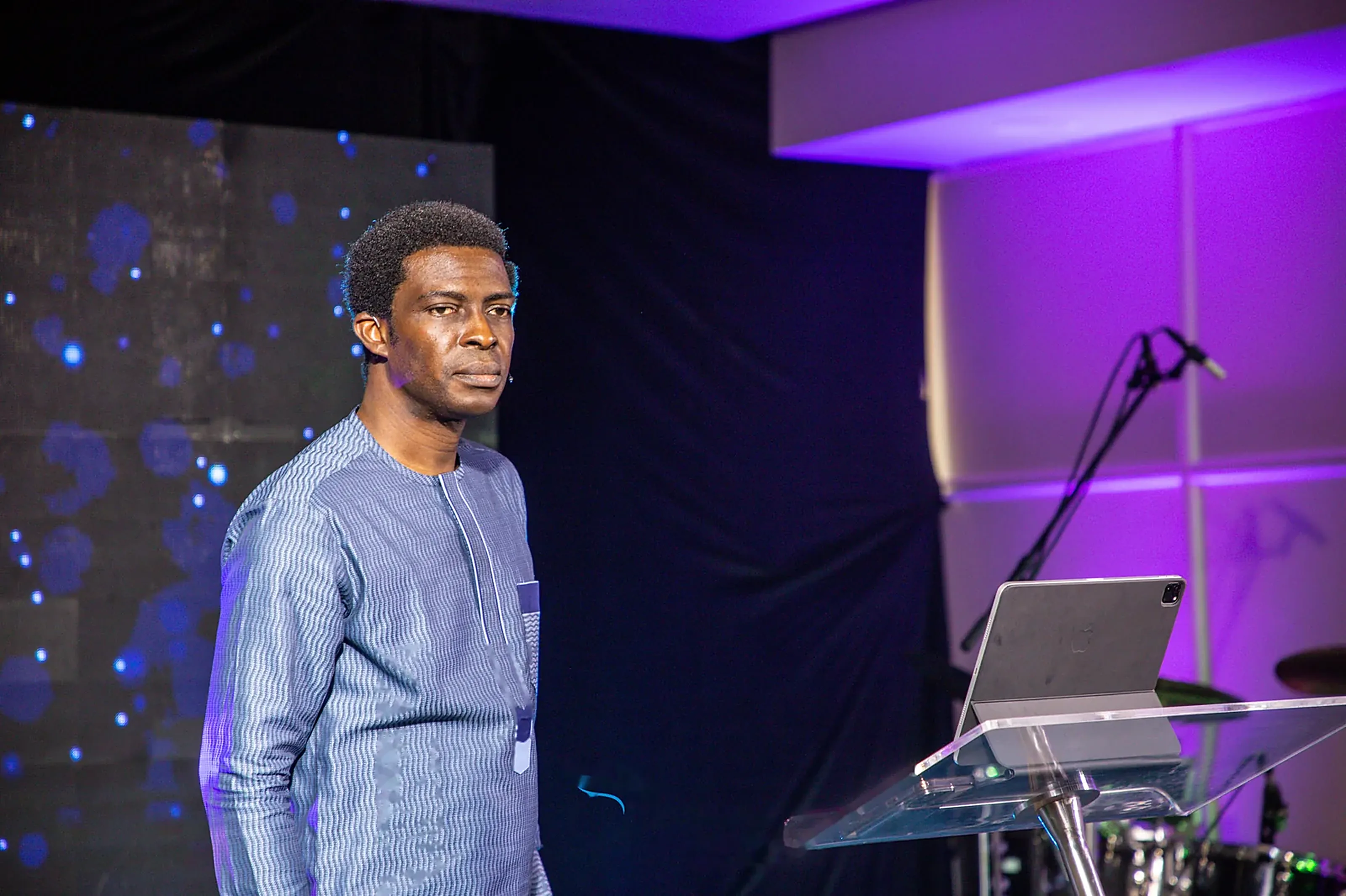 Pastor Dare Kolawole in a blue native outfit standing beside the clear lectern