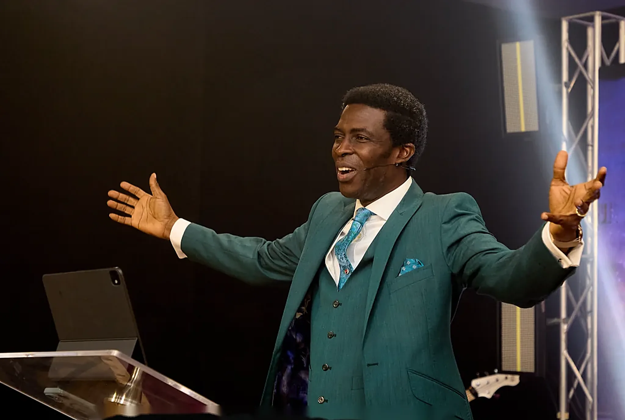 Pastor Dare Kolawole in a teal three-piece suit with arms stretched wide
