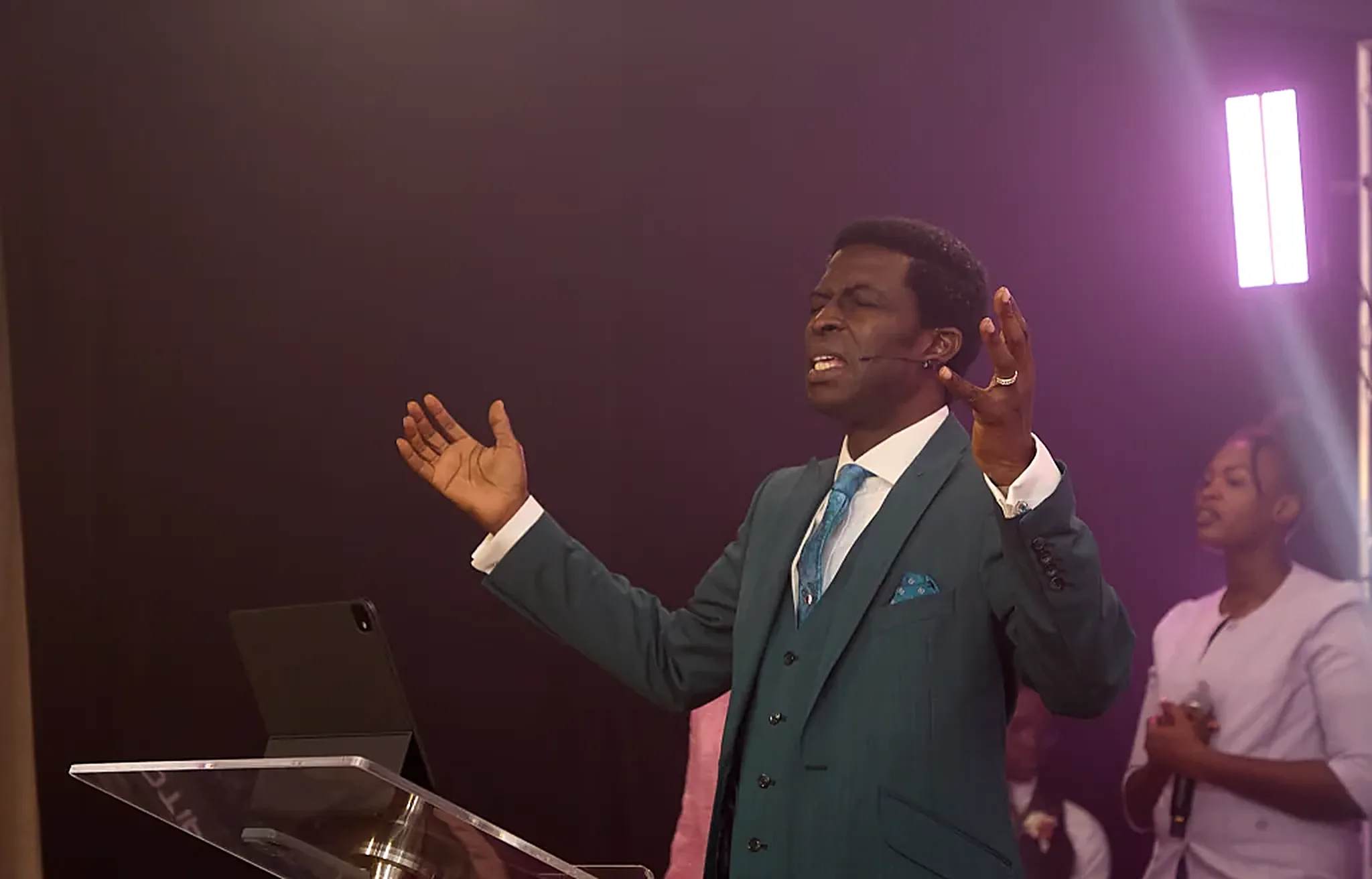 Pastor Dare Kolawole in a teal suit with arms raised in worship
